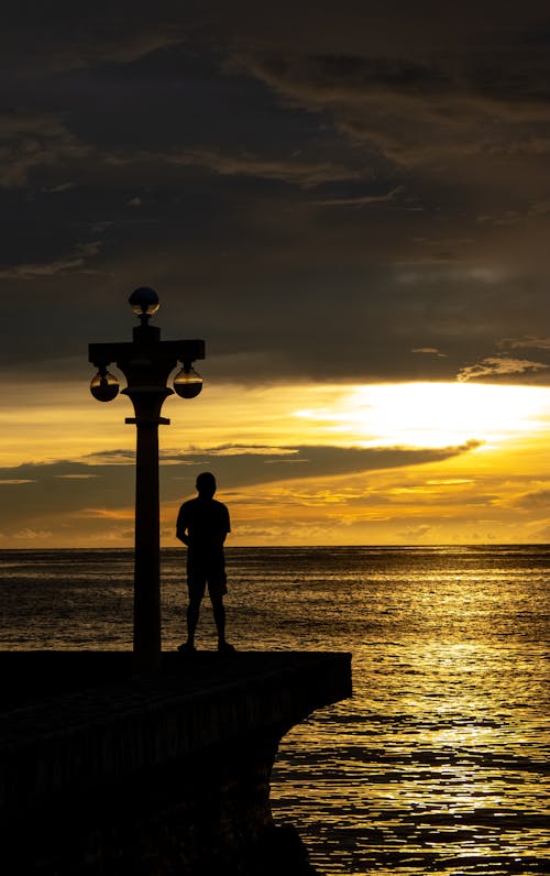 Silhouette of a Man Standing on a Pier at Sunset 