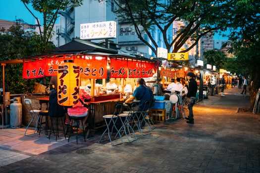 Vibrant Japanese street food market at night with illuminated stalls and people dining.