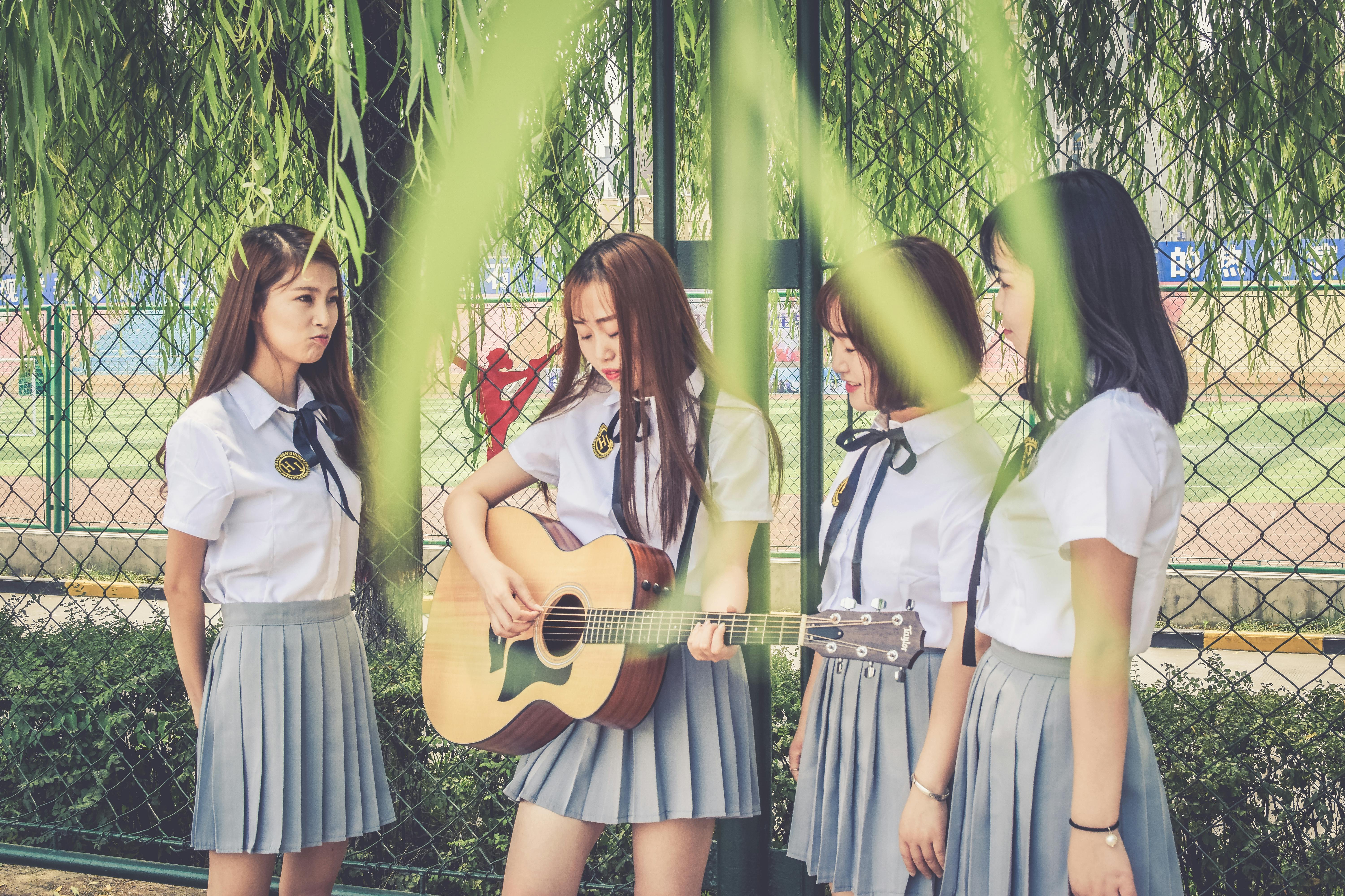 four woman singing and playing guitar near cyclone fence