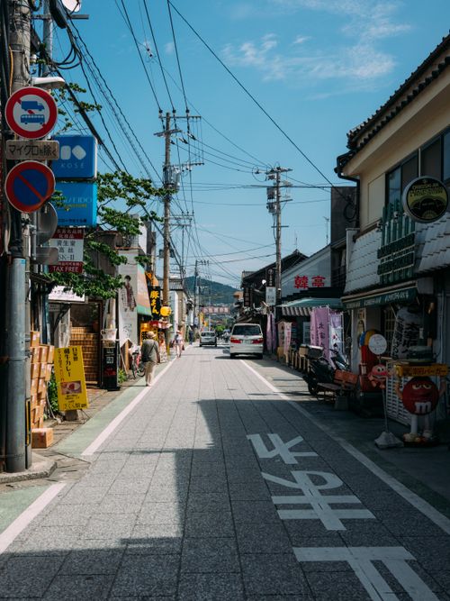 Free Street scene in a Japanese city with shops, signs, and electric posts under a blue sky. Stock Photo