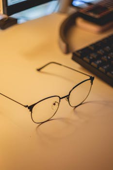 Minimalist desk with eyeglasses, keyboard, and soft lighting.
