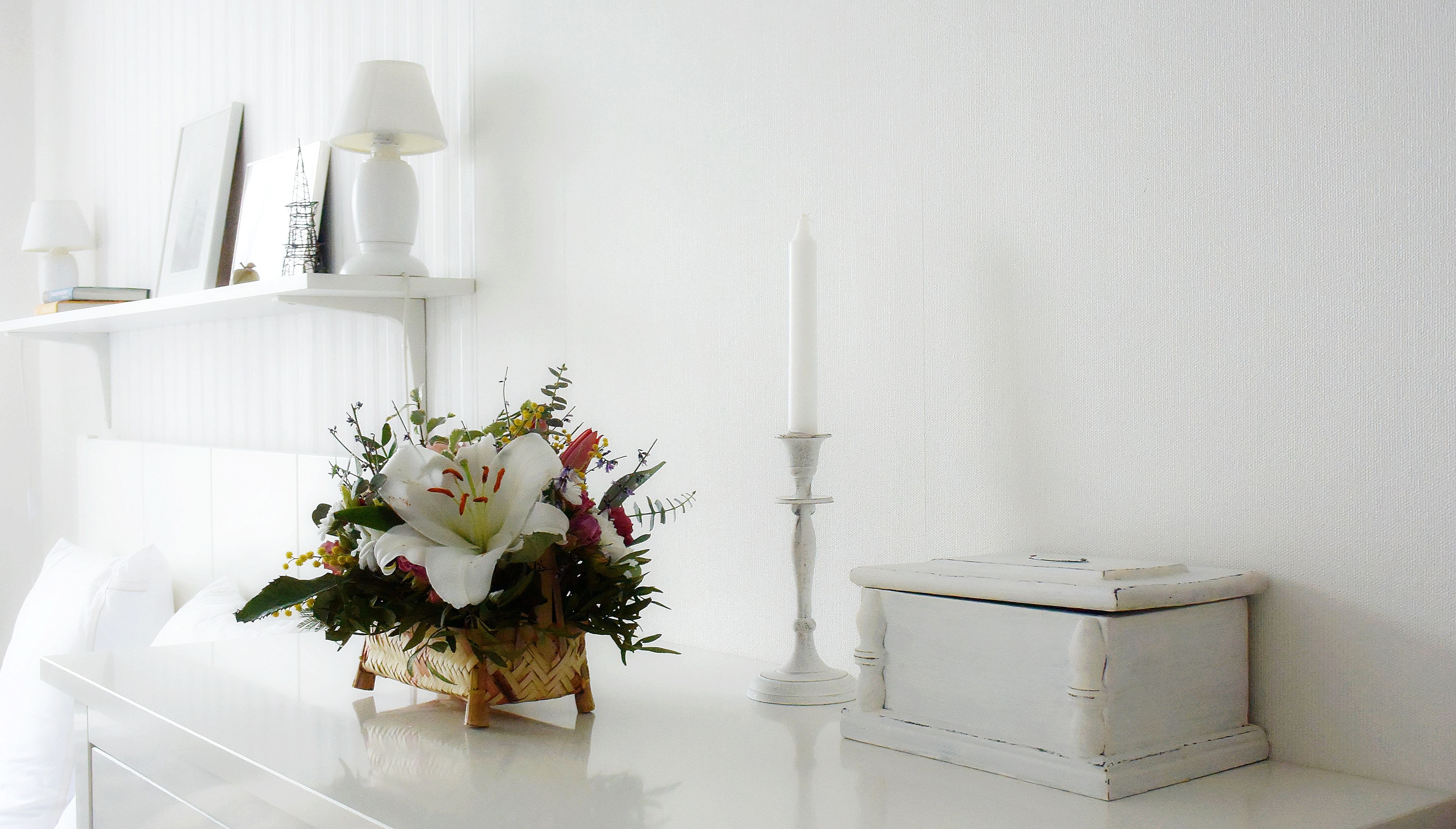 Elegant minimalist white interior with a flower arrangement and candle on a table.