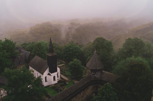 Free Drone capture of St. Martinus Church surrounded by mist and lush green forest in Germany. Stock Photo