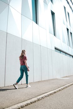 Adult woman in casual wear walking by a contemporary building facade in Jönköping, Sweden.