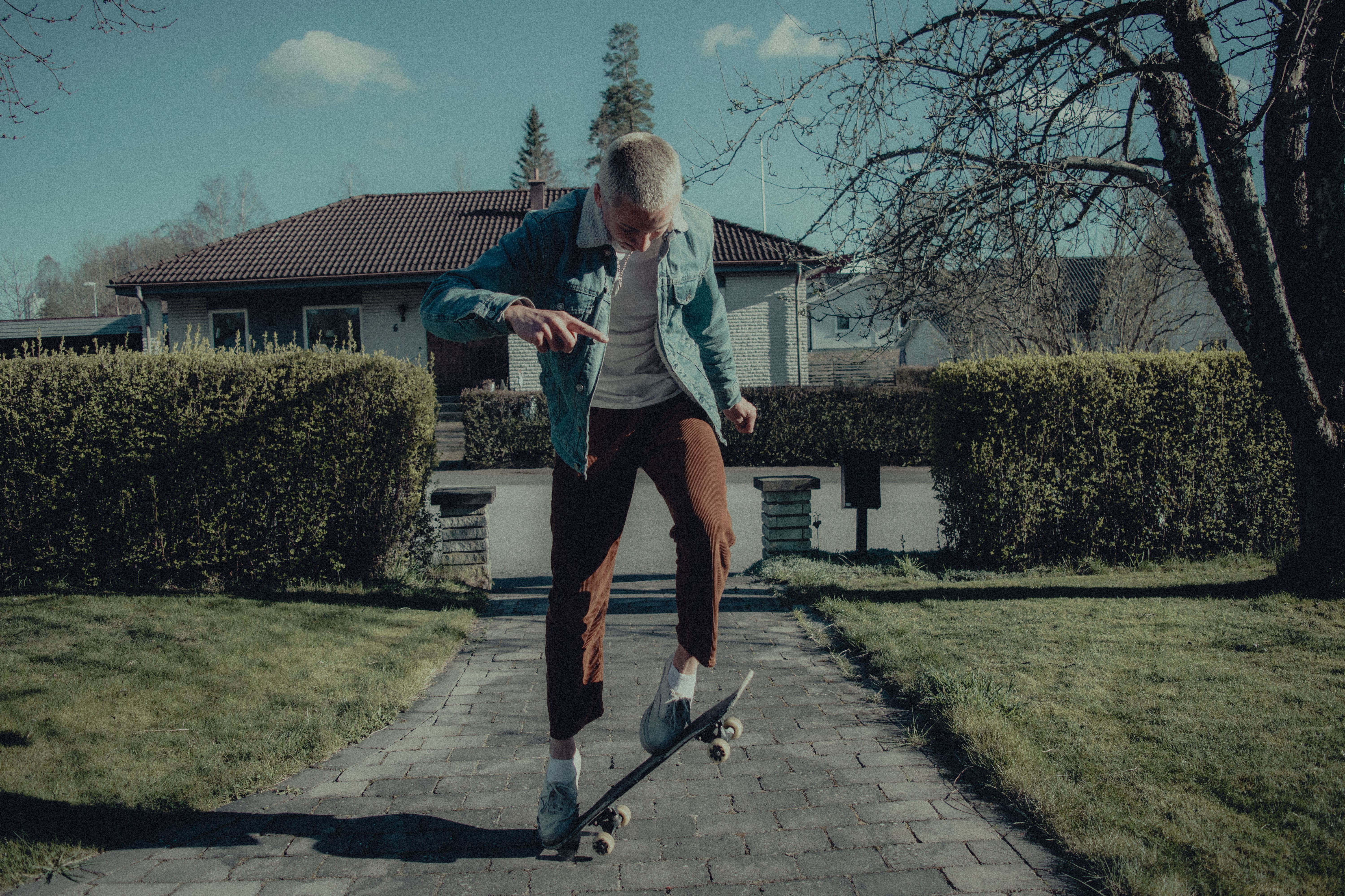 A skateboarder performs an ollie in a suburban Swedish neighborhood on a sunny day.