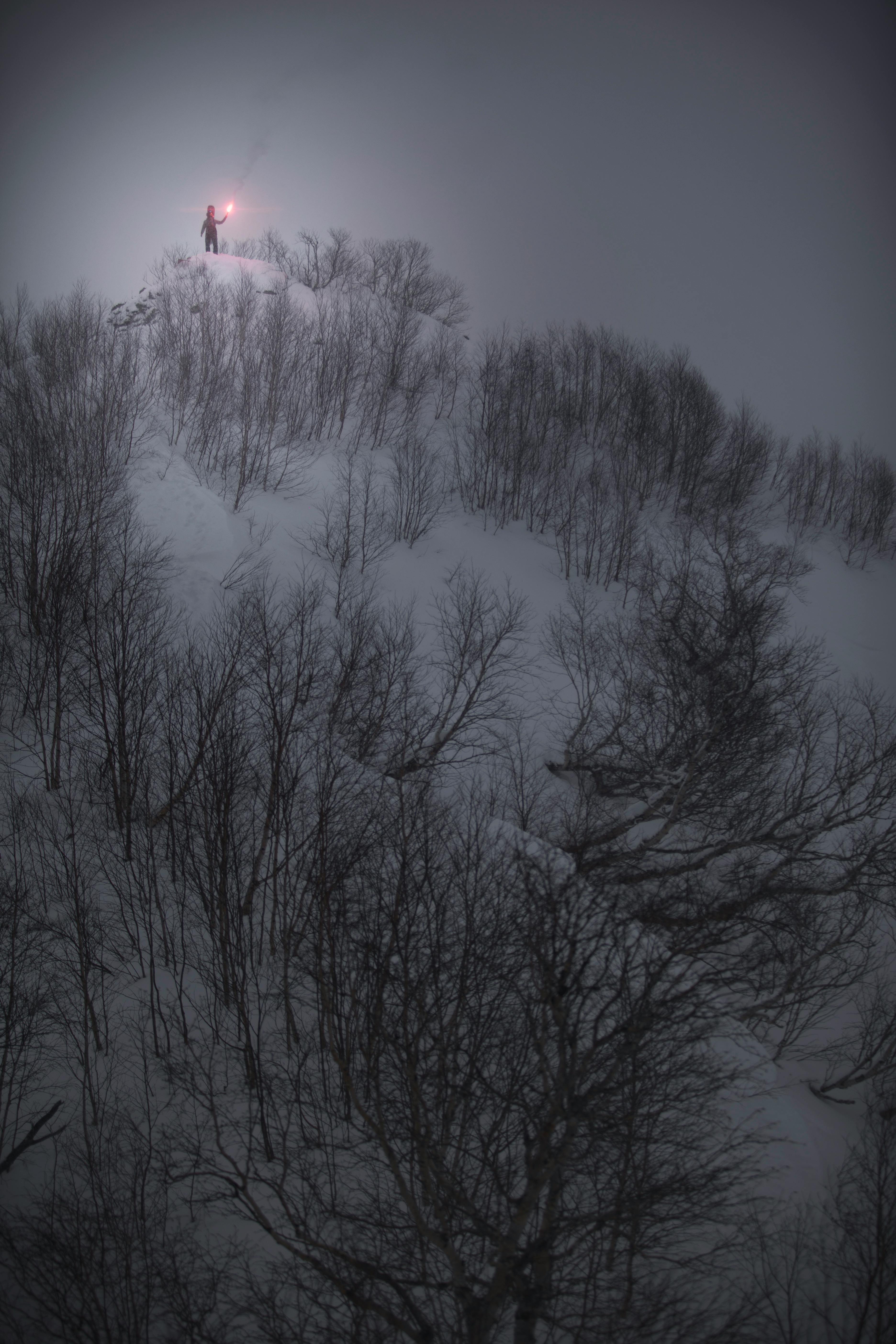 A solitary figure holds a flare atop a snowy hill in Kamchatka, Russia under a winter night sky.