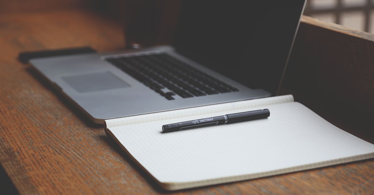 Close-up of a MacBook and notebook on a wooden desk, perfect for productivity.