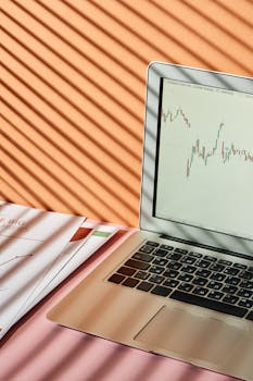 Laptop displaying stock market graph with shadows on desk, conveying a finance theme.
