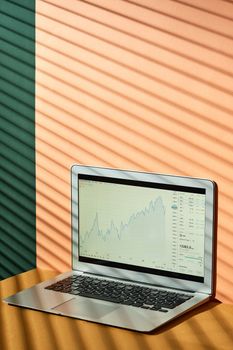 Laptop displaying stock market graph with shadow patterns on a stylish background.