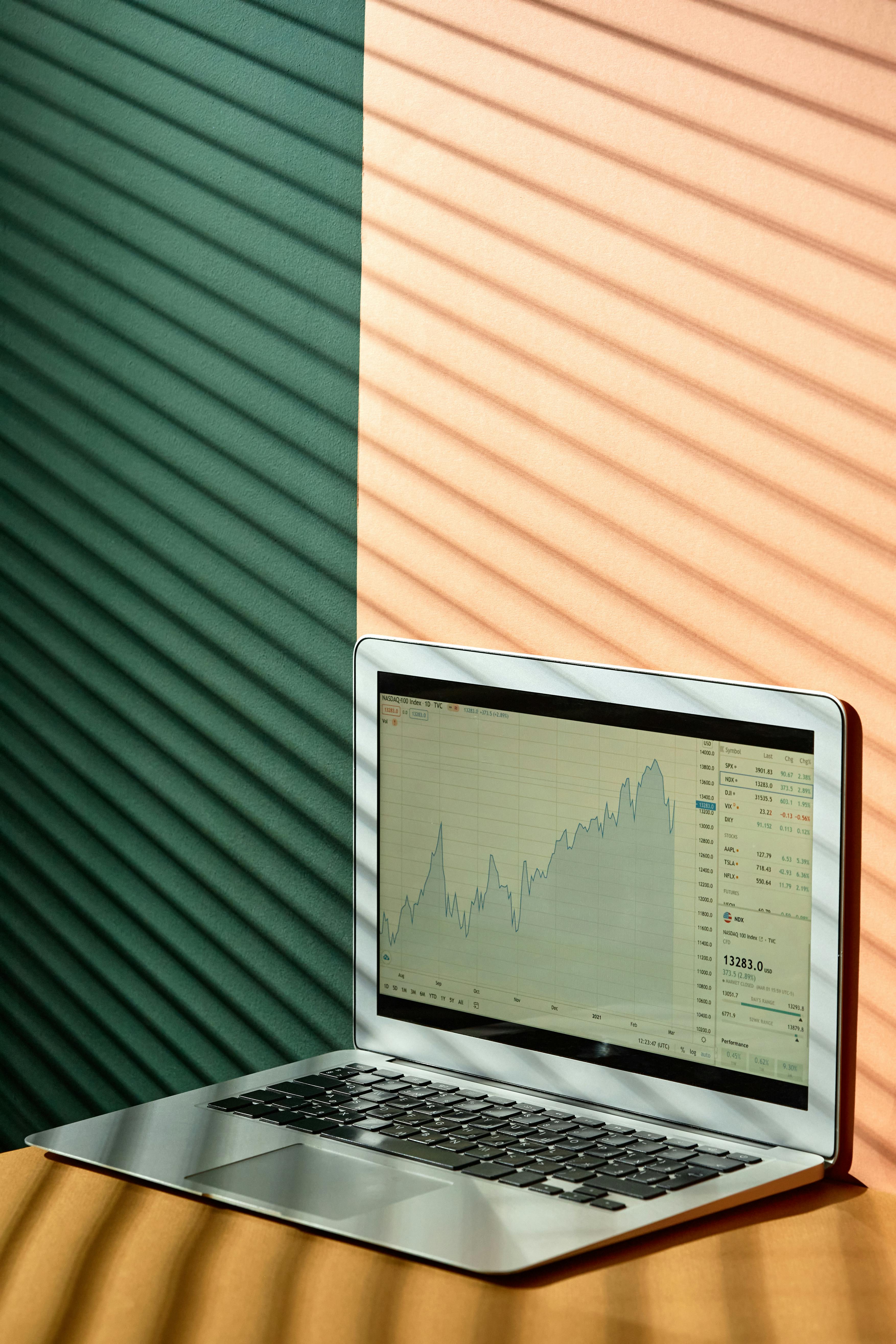 Laptop showing a stock market graph under light and shadow effect indoors.
