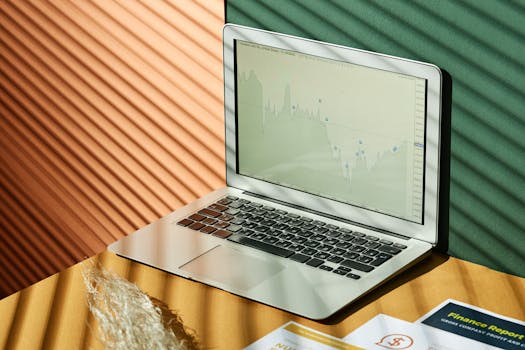 A laptop displaying analytics with financial papers on a textured surface, captured in warm lighting.