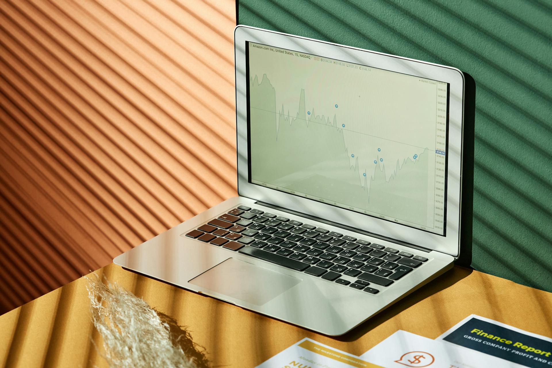 A laptop displaying analytics with financial papers on a textured surface, captured in warm lighting.