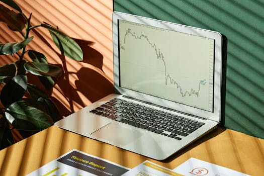 Laptop displaying a financial graph with reports, in a sunlit workspace.