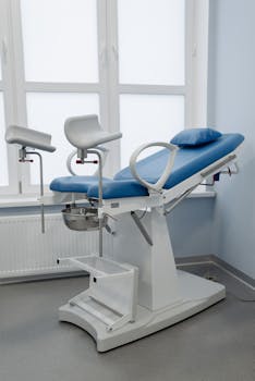 A modern gynecological chair in a sterile medical facility, featuring adjustable armrests and clean design.
