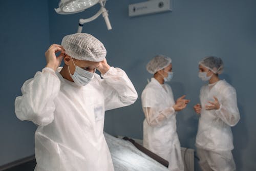 Man in Protective Suit Putting on a Face Mask Beside Two Other People