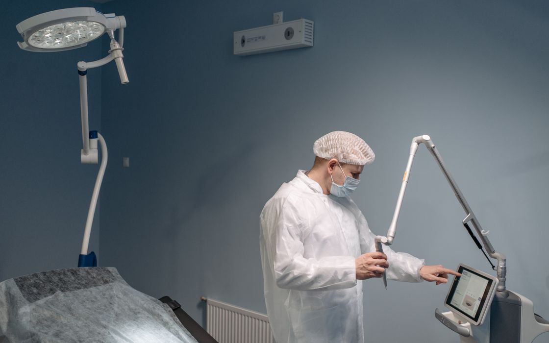 A professional doctor uses a laser machine in a modern operating room wearing protective gear.
