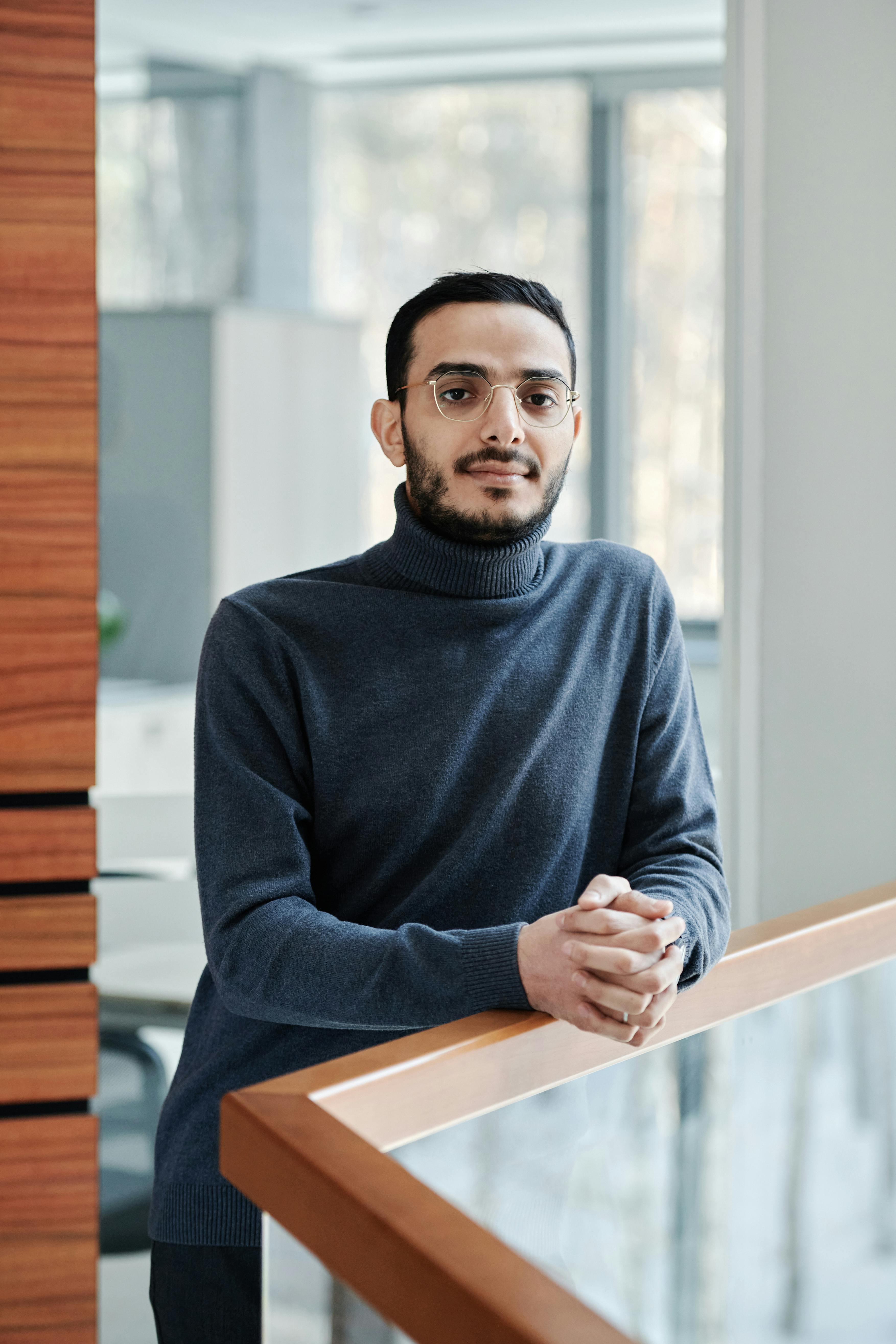 Stylish man in a turtleneck poses confidently indoors with hands together.