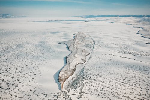 Drone view of rocky formation on icy ocean with snow under cloudy sky in wintertime