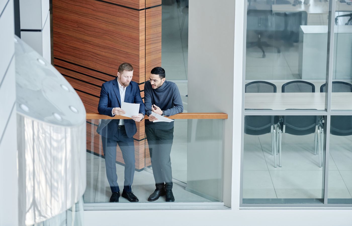 Two businessmen in a modern office building discuss documents. Professional and collaborative environment.