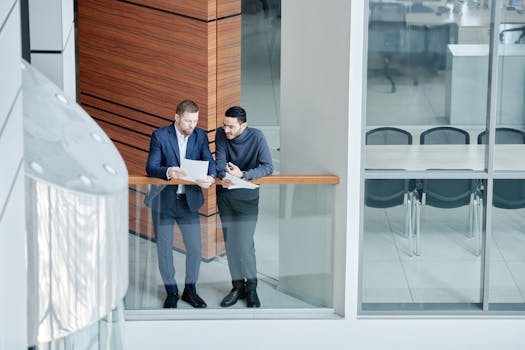 Two businessmen in a modern office building discuss documents. Professional and collaborative environment.