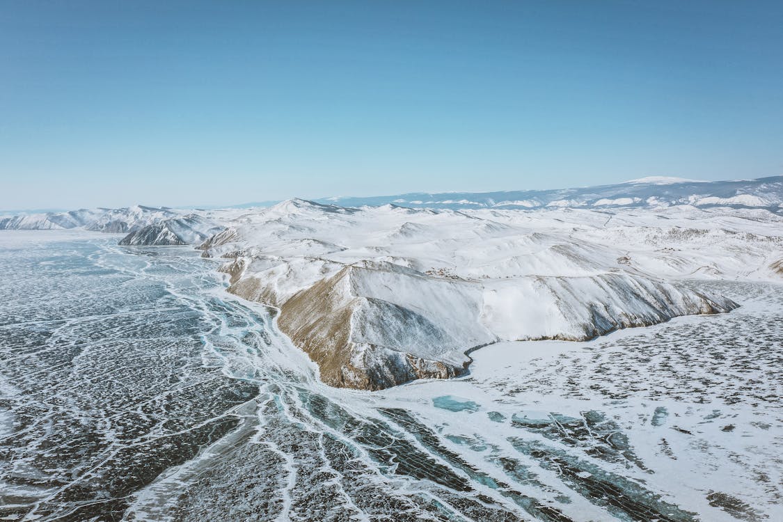 Scenic view of mounts with snow on frozen ocean under cloudy blue sky in wintertime