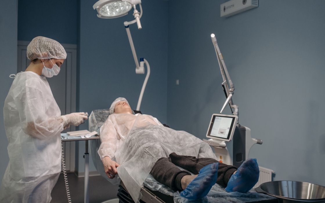 A healthcare professional performs a laser procedure on a female patient in a sterile operating room.