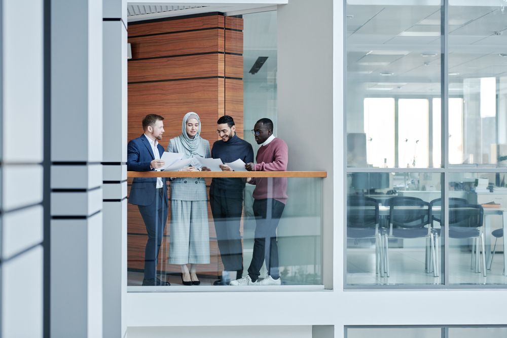 A group of colleagues collaborating around a table in a bright glass-walled office