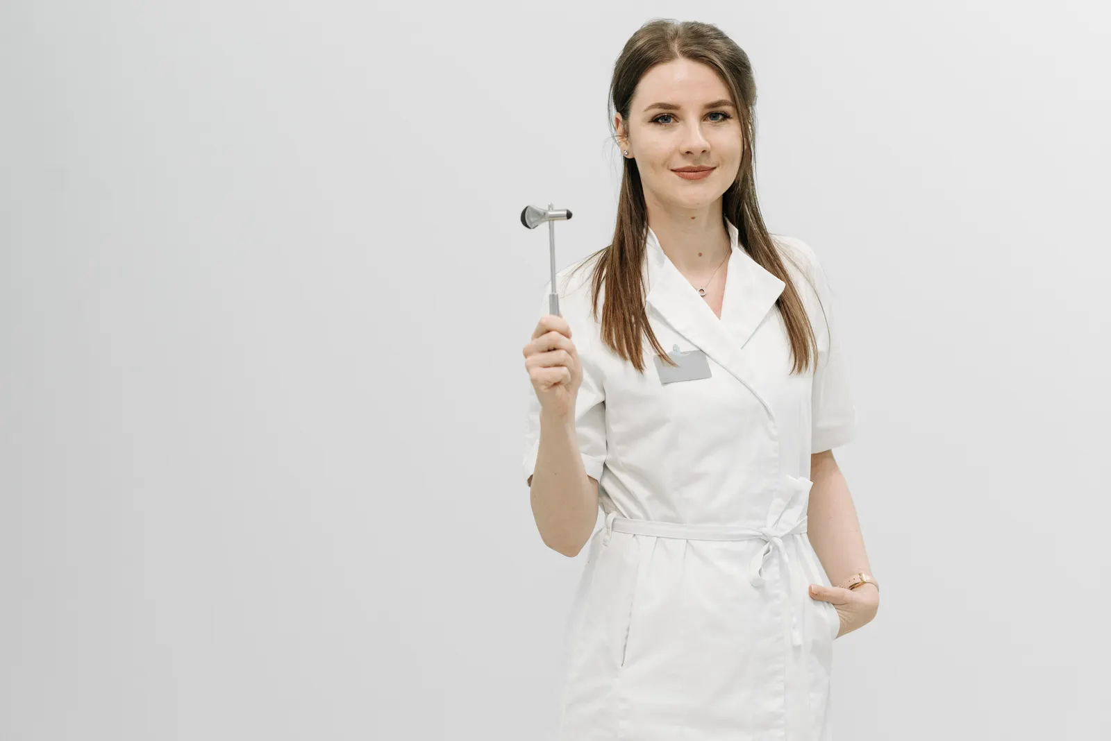 Female healthcare professional posing confidently in a white coat holding a reflex hammer.