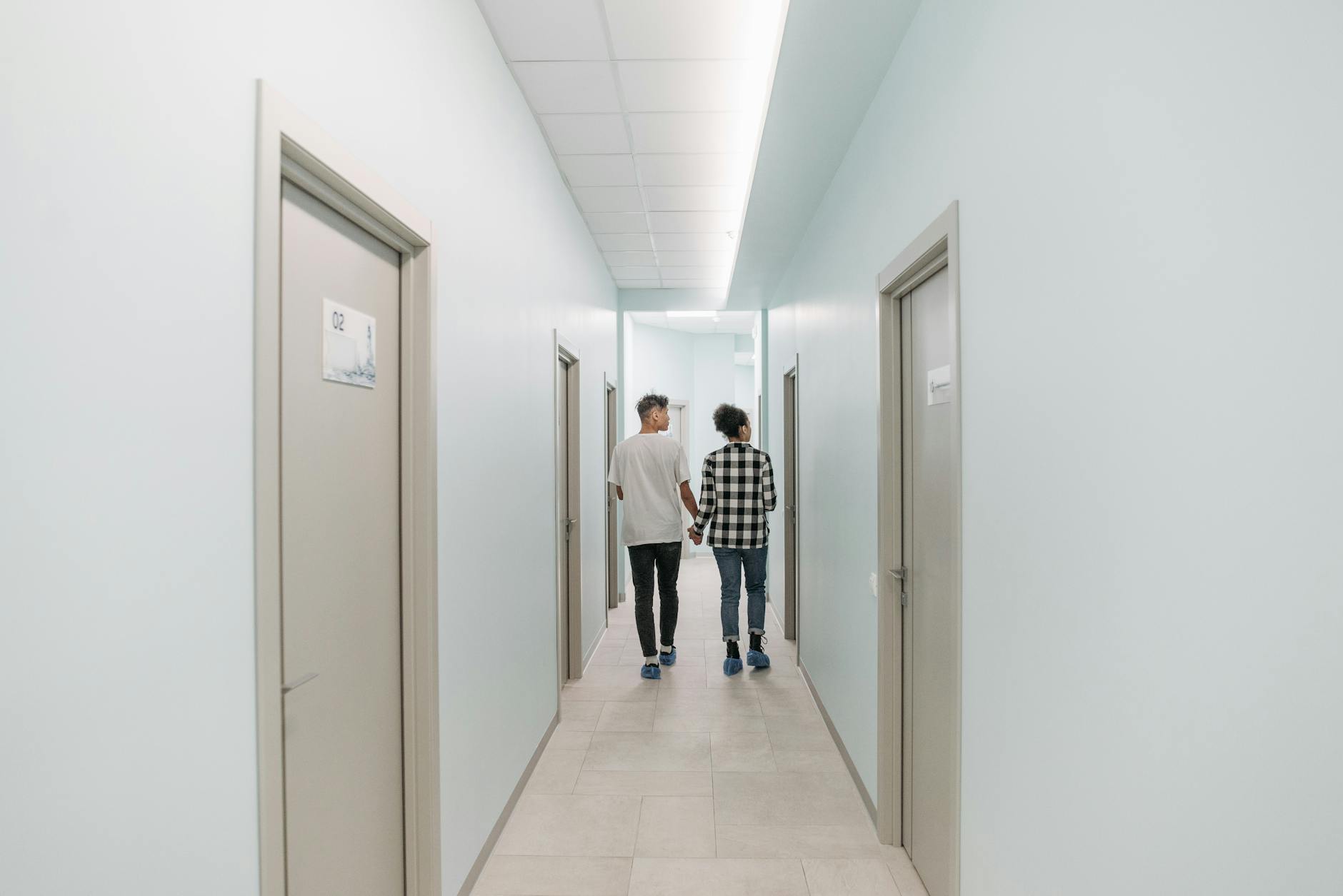 A couple holding hands walking down a clinic hallway indoors, conveying support and companionship.