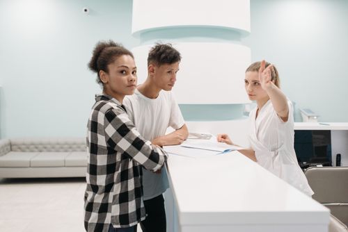 Free Two patients at hospital reception desk interacting with receptionist in white attire. Stock Photo