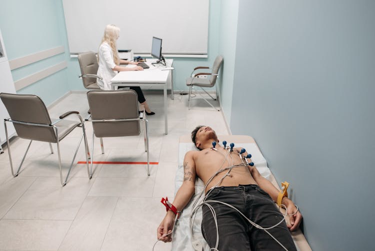 A Medical Practitioner Working With Her Computer While A Patient Is Lying On The Clinic Bed