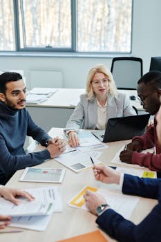 A diverse group of colleagues engaged in a meeting around a table with documents.