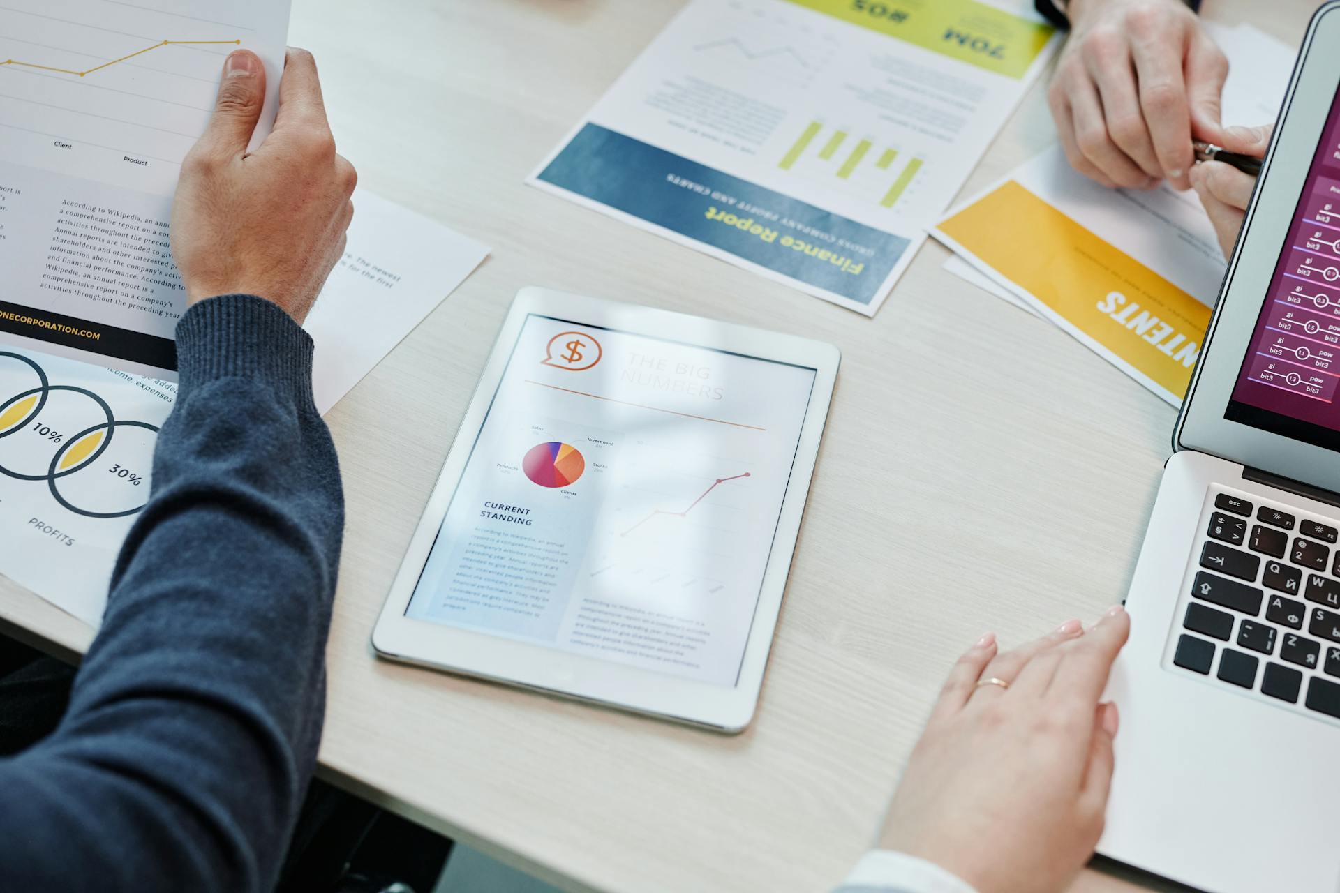 Top view of a business meeting table with digital devices and financial documents, showing collaboration.