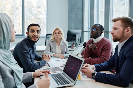 Diverse group of professionals engaged in a conference room discussion with laptops and documents.