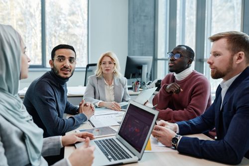 Free Diverse group of professionals engaged in a conference room discussion with laptops and documents. Stock Photo
