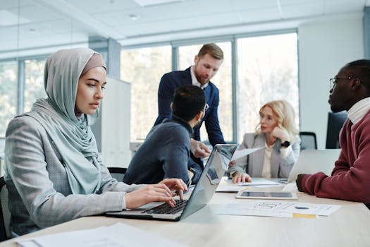 A diverse group of professionals collaborating in a modern office setting with laptops and documents.