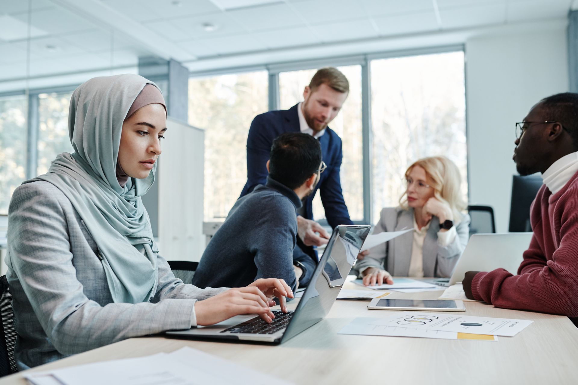 A diverse group of professionals collaborating in a modern office setting with laptops and documents.