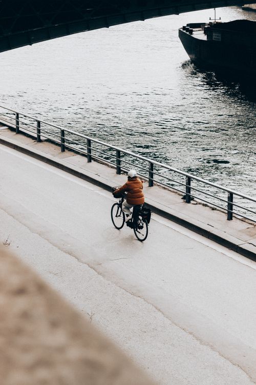 Free From above back view of anonymous bicyclist riding bike on fenced bridge above lake with ship Stock Photo