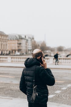 Man in padded jacket using smartphone on city street during winter.