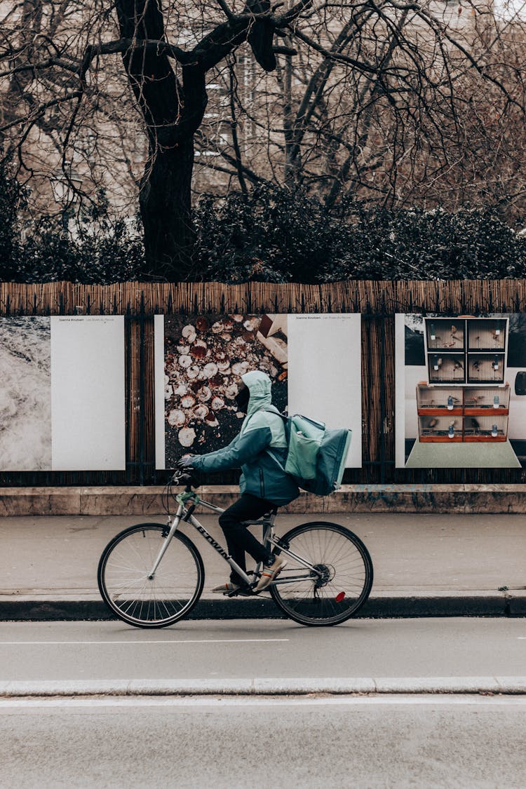 Unrecognizable Delivery Person Riding Bike On Urban Road Against Photos