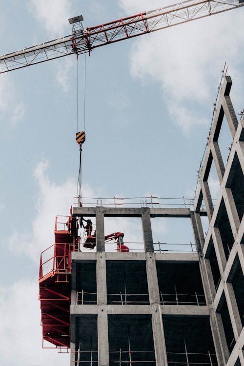 From below of unrecognizable male foremen standing on half built building during work at construction site against cloudy blue sky