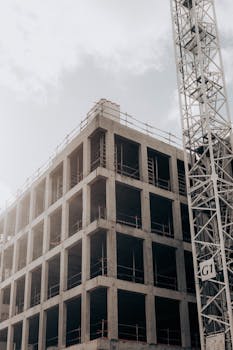 Concrete structure of a multistory building with adjacent crane under cloudy sky.