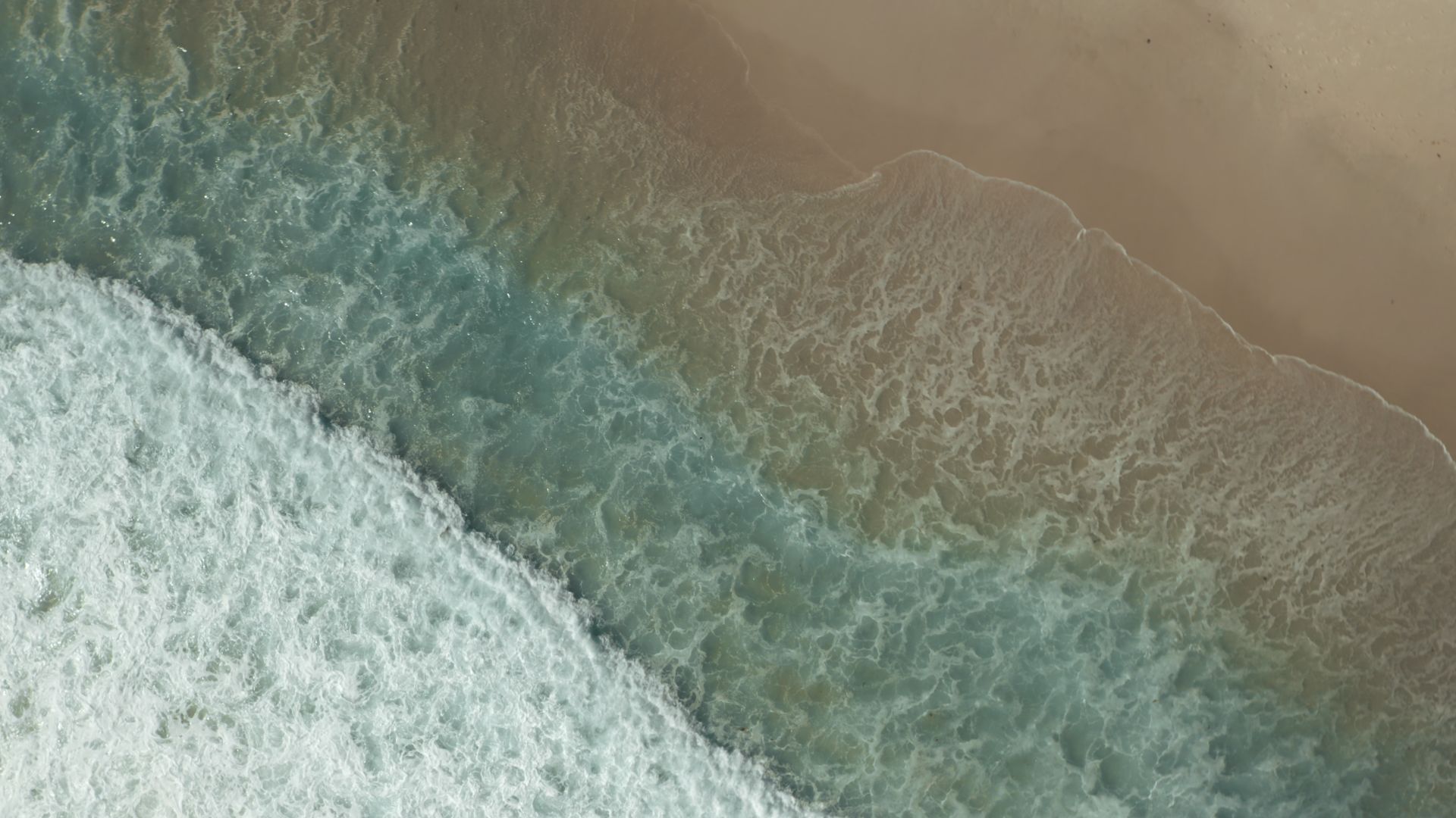 Aerial view of ocean waves crashing onto a sandy beach in Cape Town, South Africa. Vibrant coastal scenery.