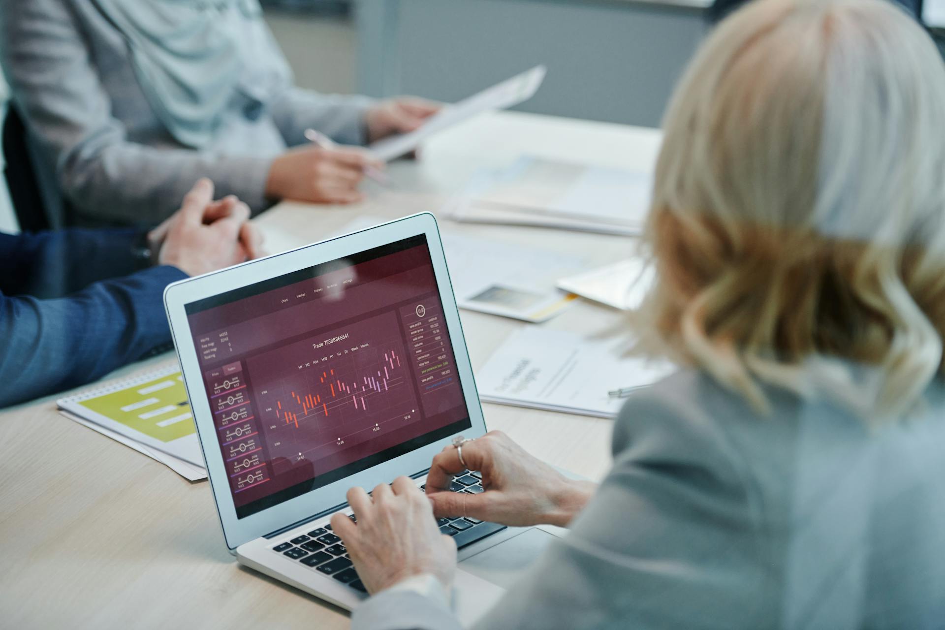 Business professionals analyzing stock market data on a laptop during a meeting.