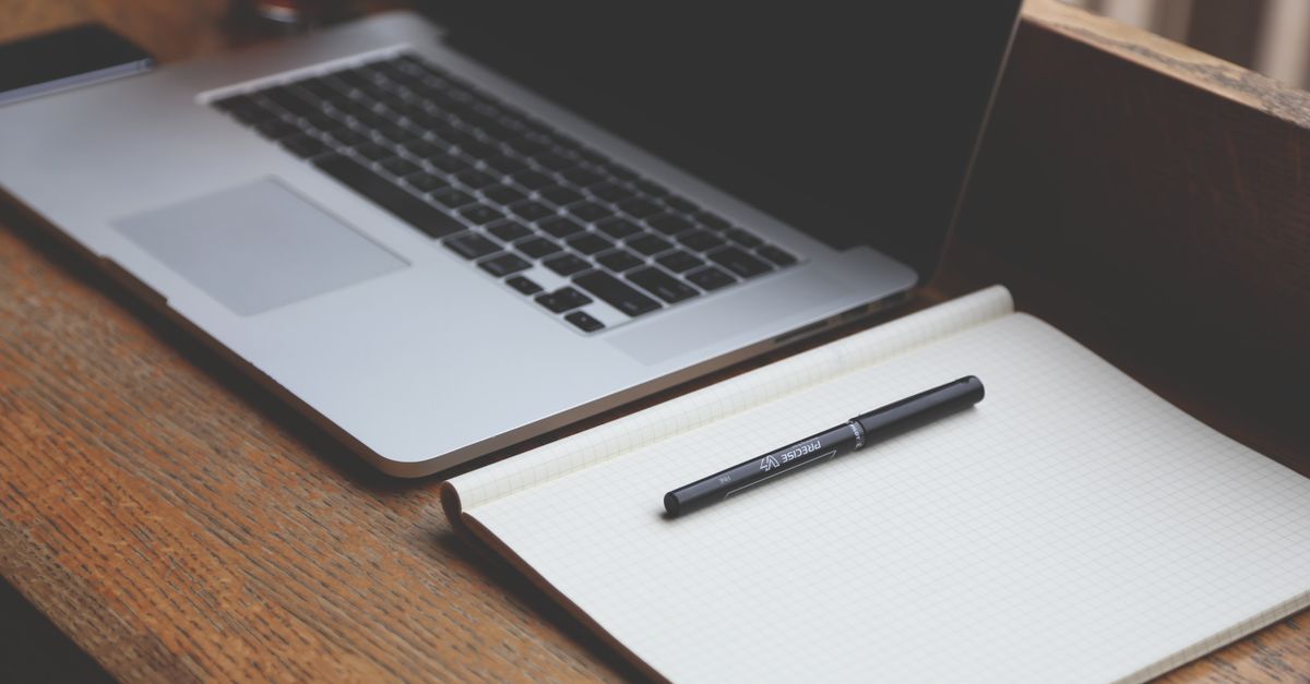 A clean office workspace with a laptop and notebook side by side — the focused setup an invoice gets written from.