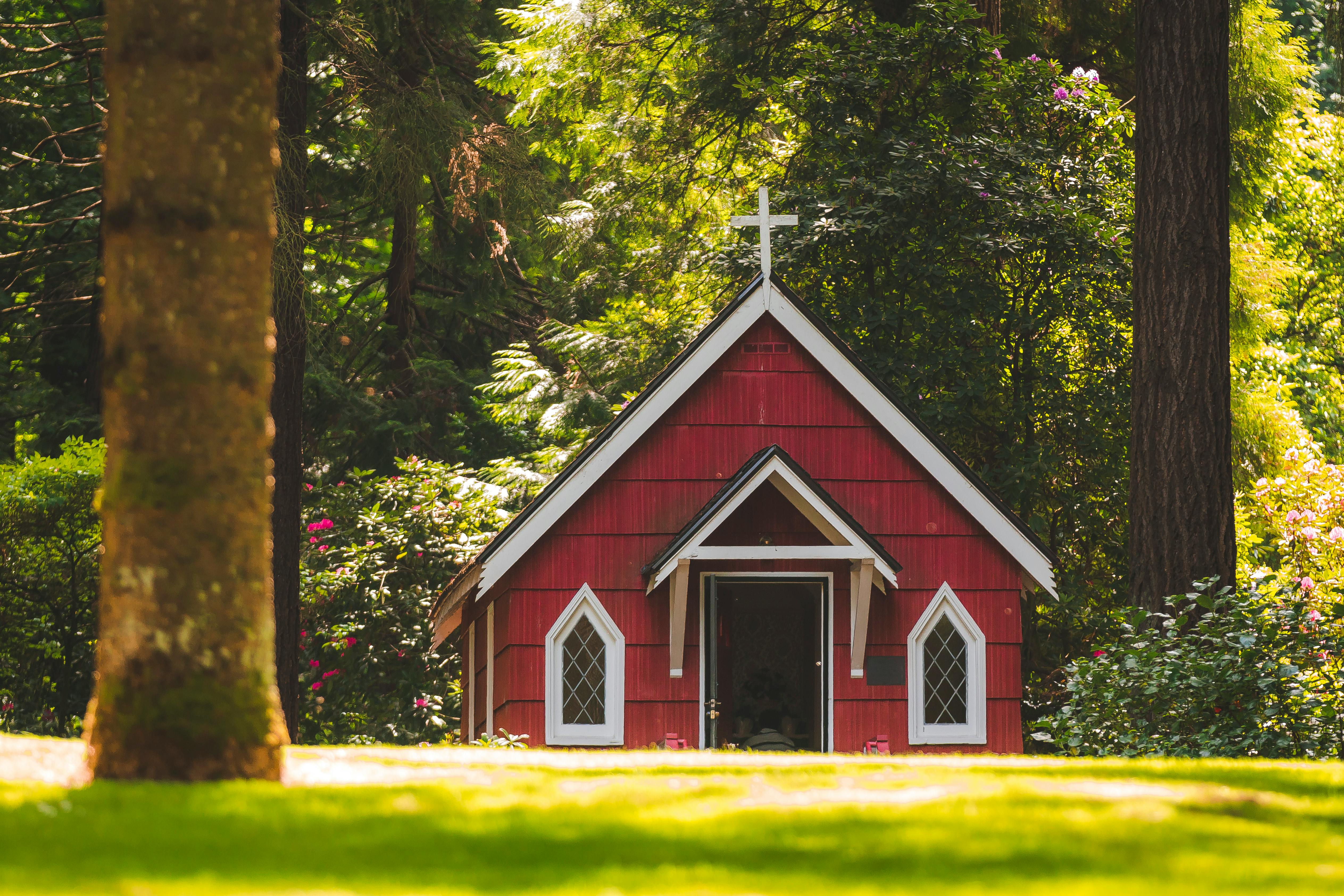 Red chapel on a grassy field with trees. | Photo: Pexels