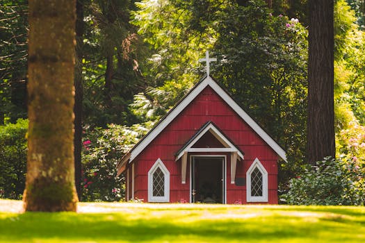 A small red chapel with a white cross nestled in a lush green forest in Portland, Oregon.