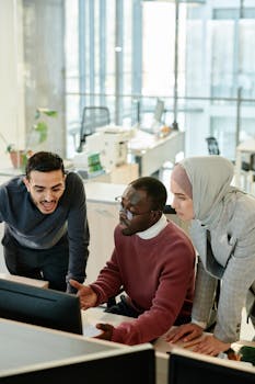 A diverse group of colleagues working together, focusing on a computer screen in a modern office.