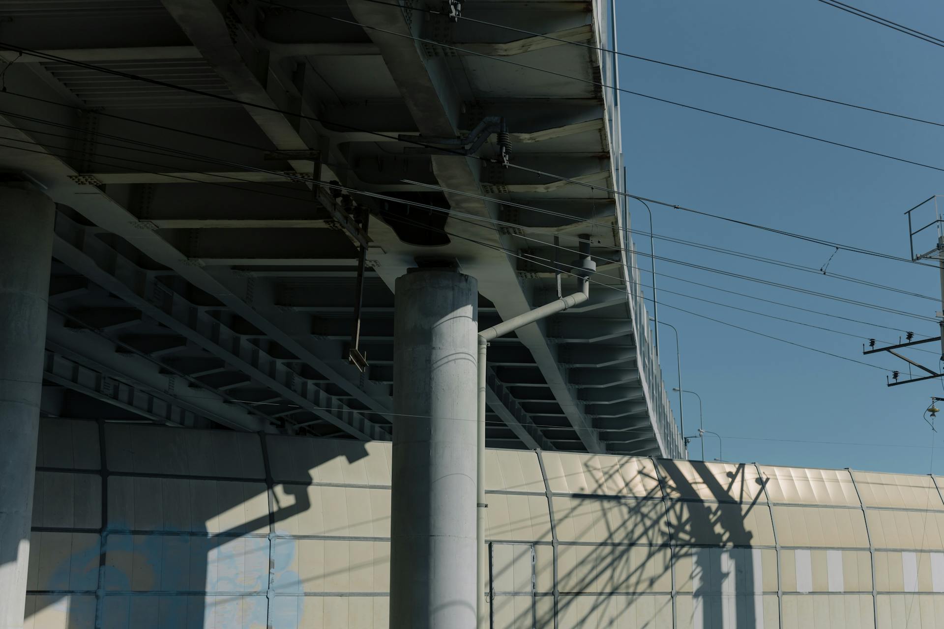 View of an industrial overpass with electrical wires and infrastructure against a clear blue sky.