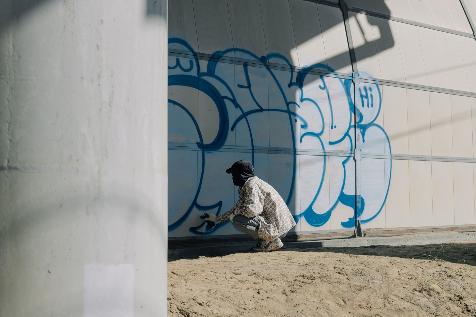 Street artist using spray paint for a graffiti mural on a concrete wall in urban setting.